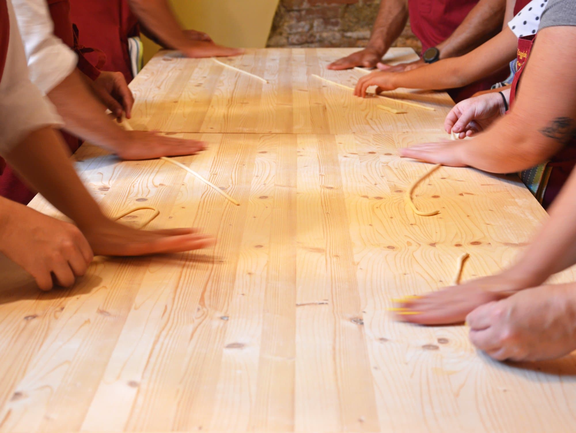 Diverse mani che modellano i Pici, la pasta fresca toscana, su un tavolo di legno
