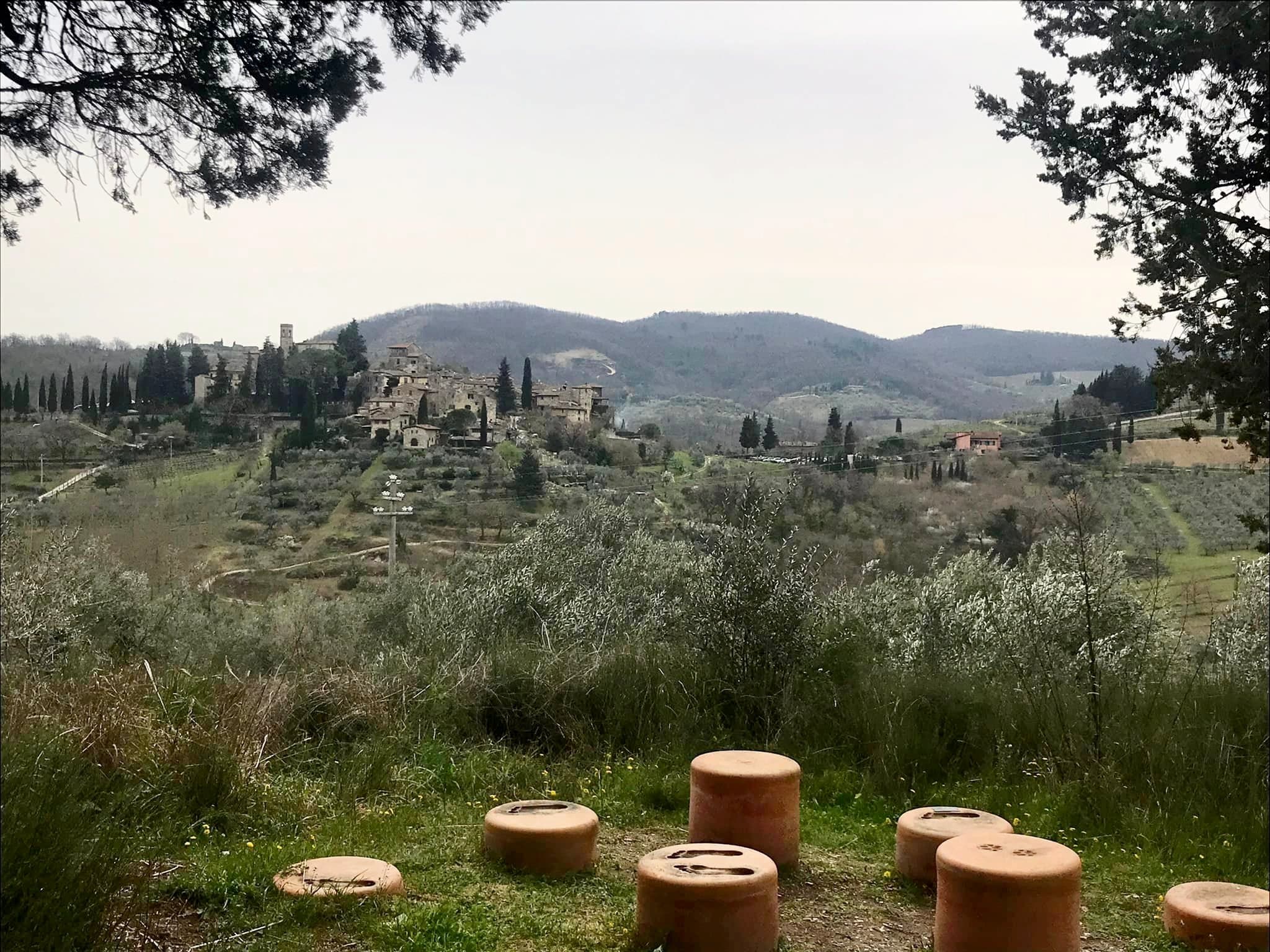 Panorama delle colline del Chianti con il borgo medievale di Montefioralle sullo sfondo, ulivi e cipressi nel paesaggio toscano, anfore in terracotta in primo piano