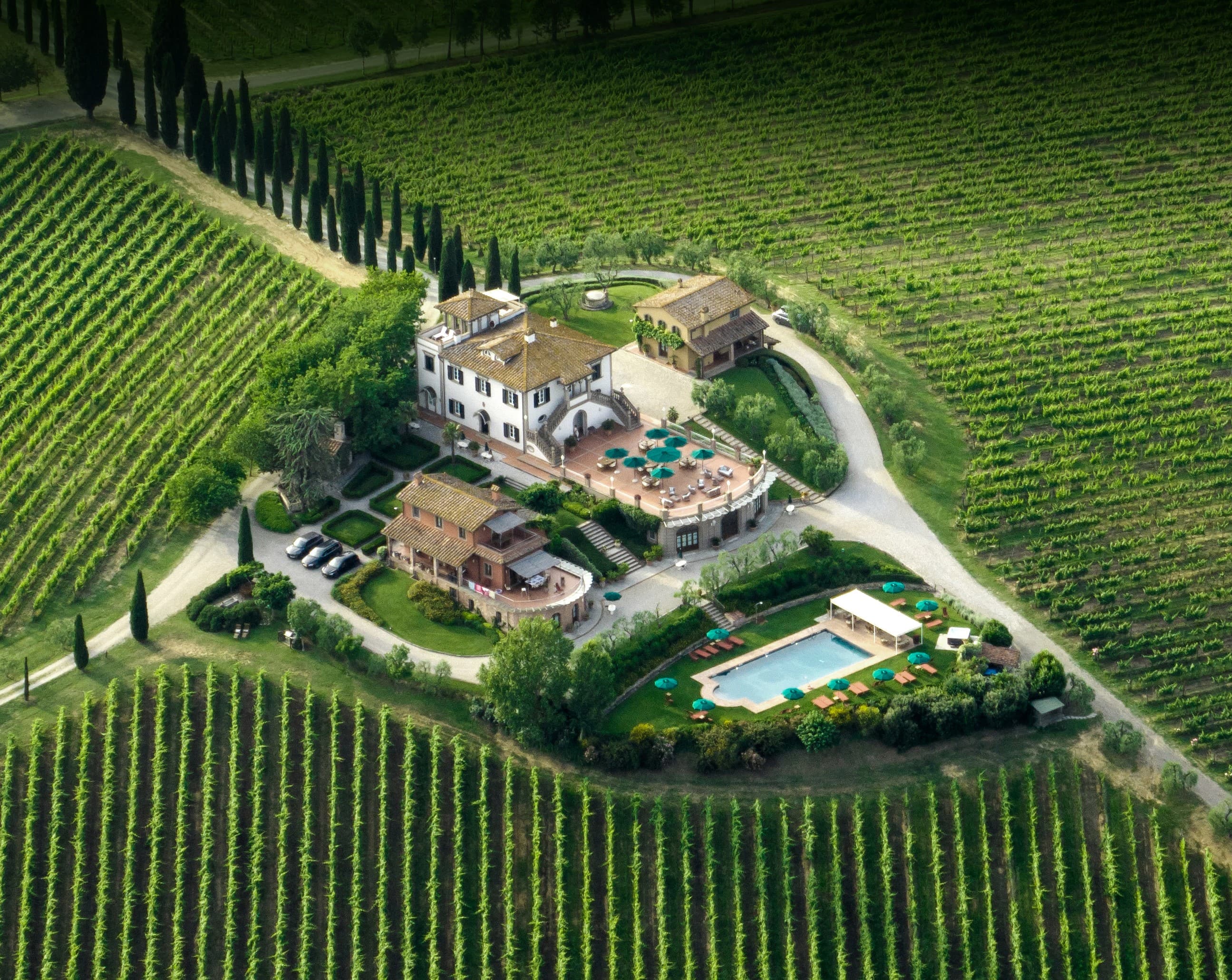 Veduta aerea della villa di Poggio al Casone circondata da vigneti, piscina e giardini