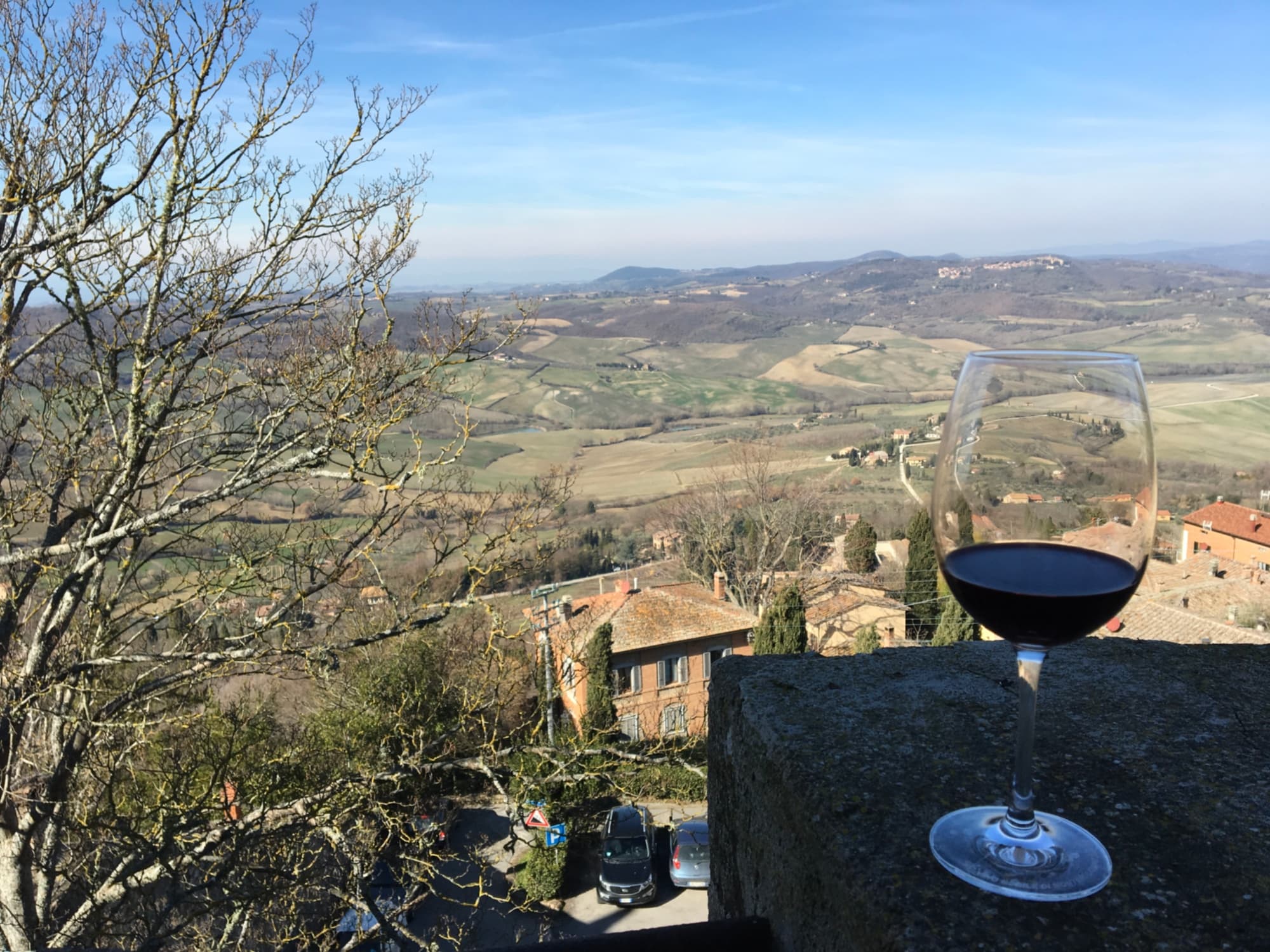 Un verre de rouge au premier plan avec le paysage toscan typique à l’arrière-plan. Le Vin est un Nobile di Montepulciano.