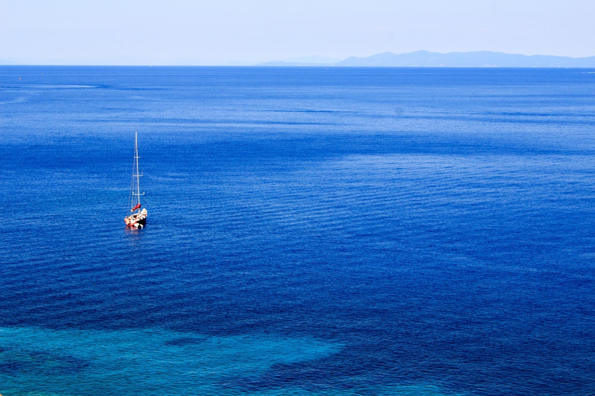 Una barca a vela ormeggiata nelle acque cristalline vicino alla costa dell’Isola del Giglio