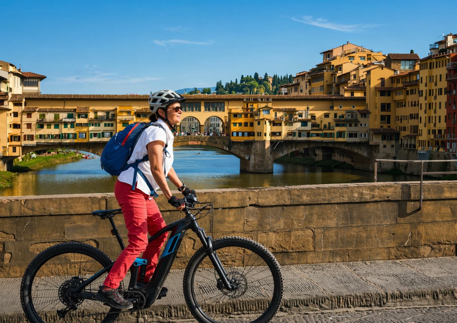 Woman riding an electric mountain bike crosses a bridge in Florence with a panoramic view of the Ponte Vecchio and the Arno River