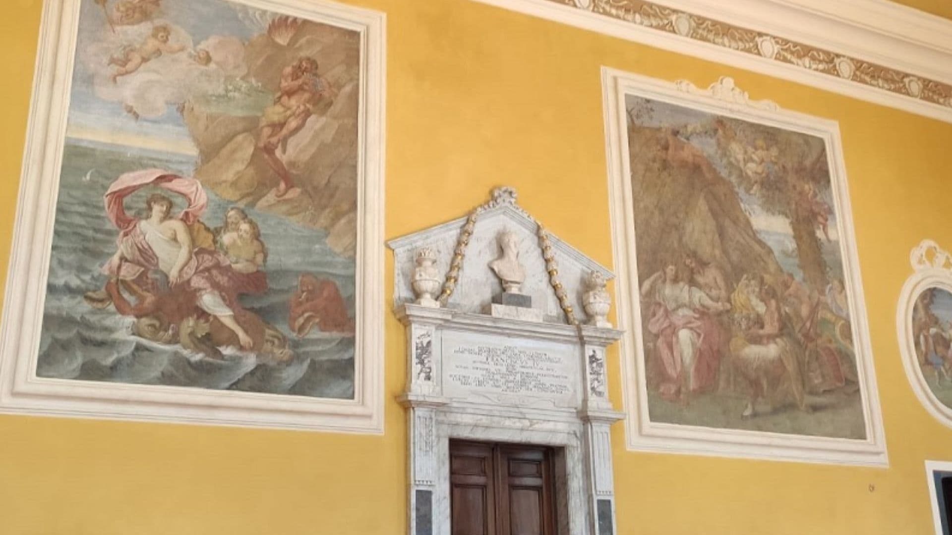 Interno del Castello di Pallerone con grande camino marmoreo, pareti gialle e ampi affreschi raffiguranti scene mitologiche.