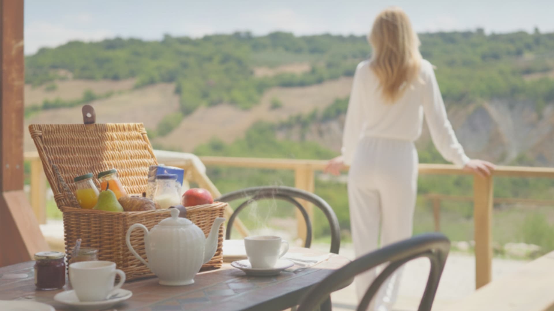 Woman having breakfast on the glamping tent veranda overlooking the Maremma hills.
