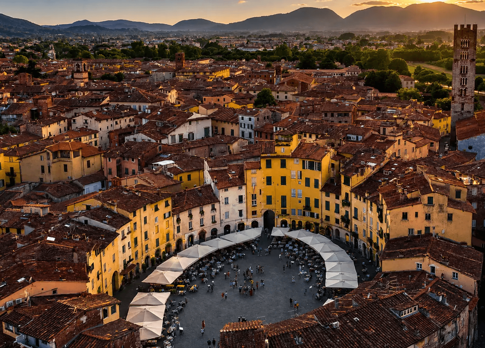 Panoramic view of Lucca from above at sunset, with terracotta roofs, the Piazza dell'Anfiteatro, and the Tuscan hills in the background