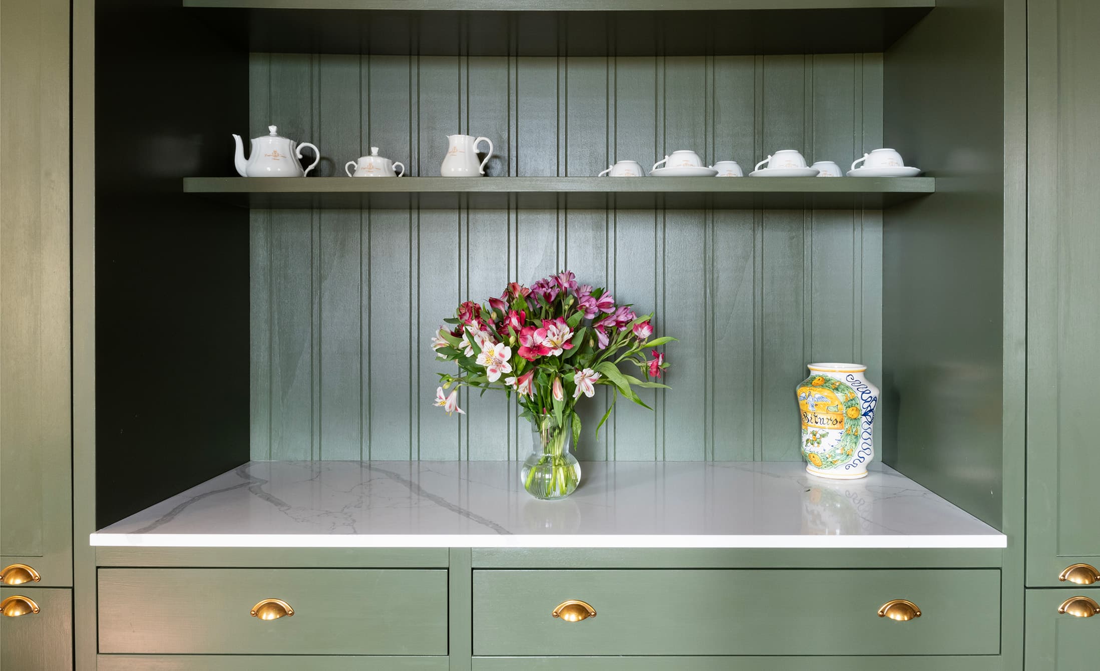 Sage green shelf with ceramic tea set, flower vase and decorated pitcher