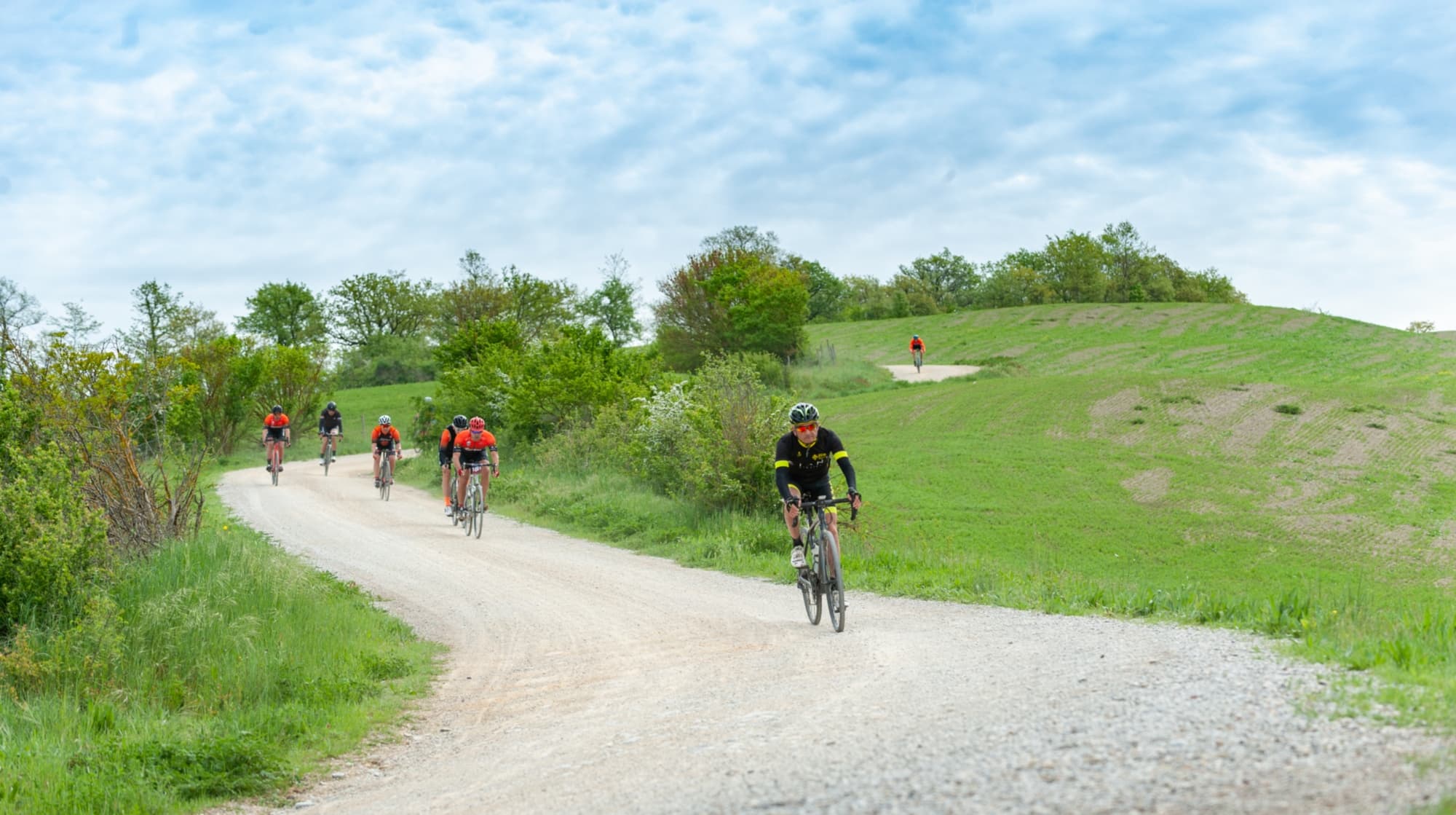 Ciclisti gravel partecipano alla Nova Eroica pedalando su una strada bianca tra colline verdi e vegetazione