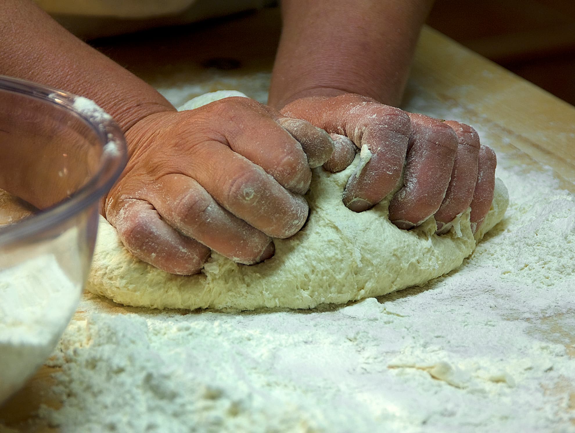 Mani che impastano la pasta fresca su un piano infarinato