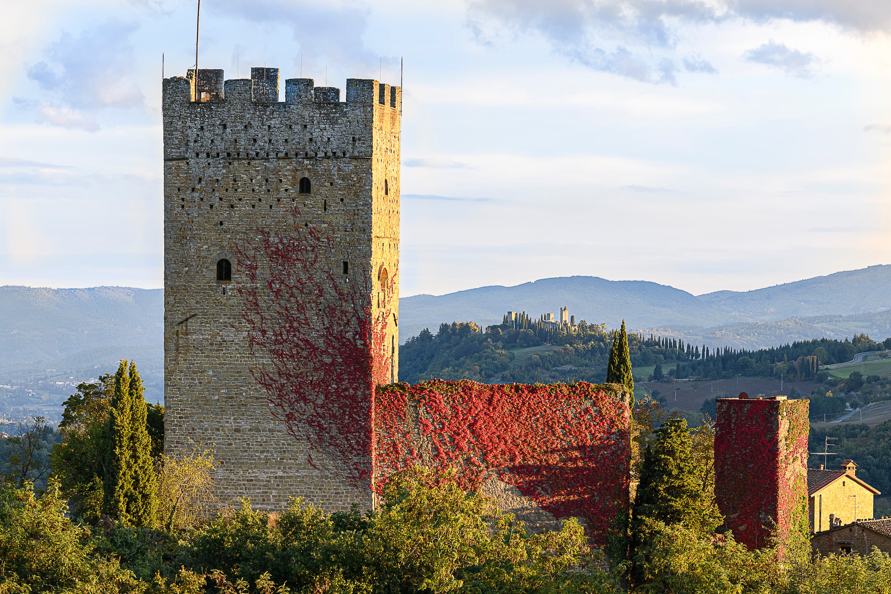 Medieval tower of Porciano Castle with walls covered in red autumnal ivy, Tuscan Casentino hills in the background