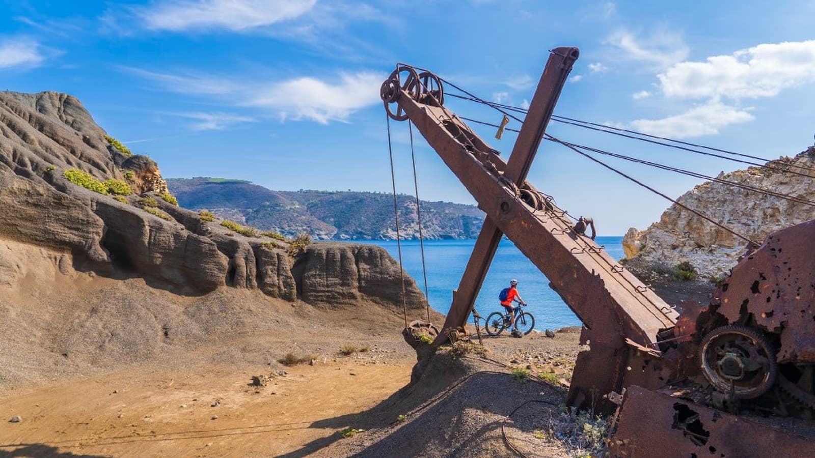 E-bike cyclist next to a rusty industrial crane in the mining area of Elba Island