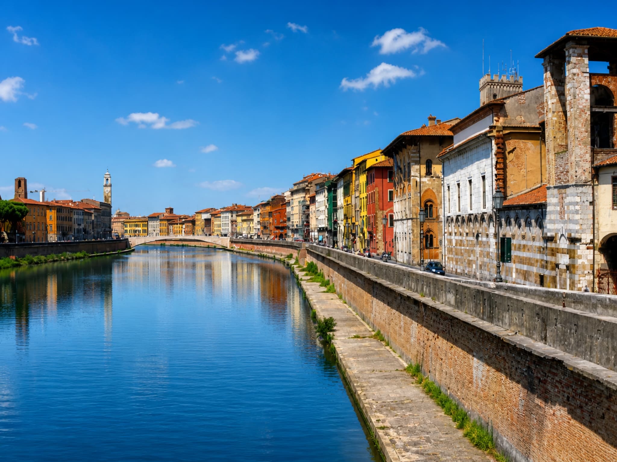 Lungarno di Pisa con palazzi colorati riflessi nelle acque dell'Arno in una giornata soleggiata
