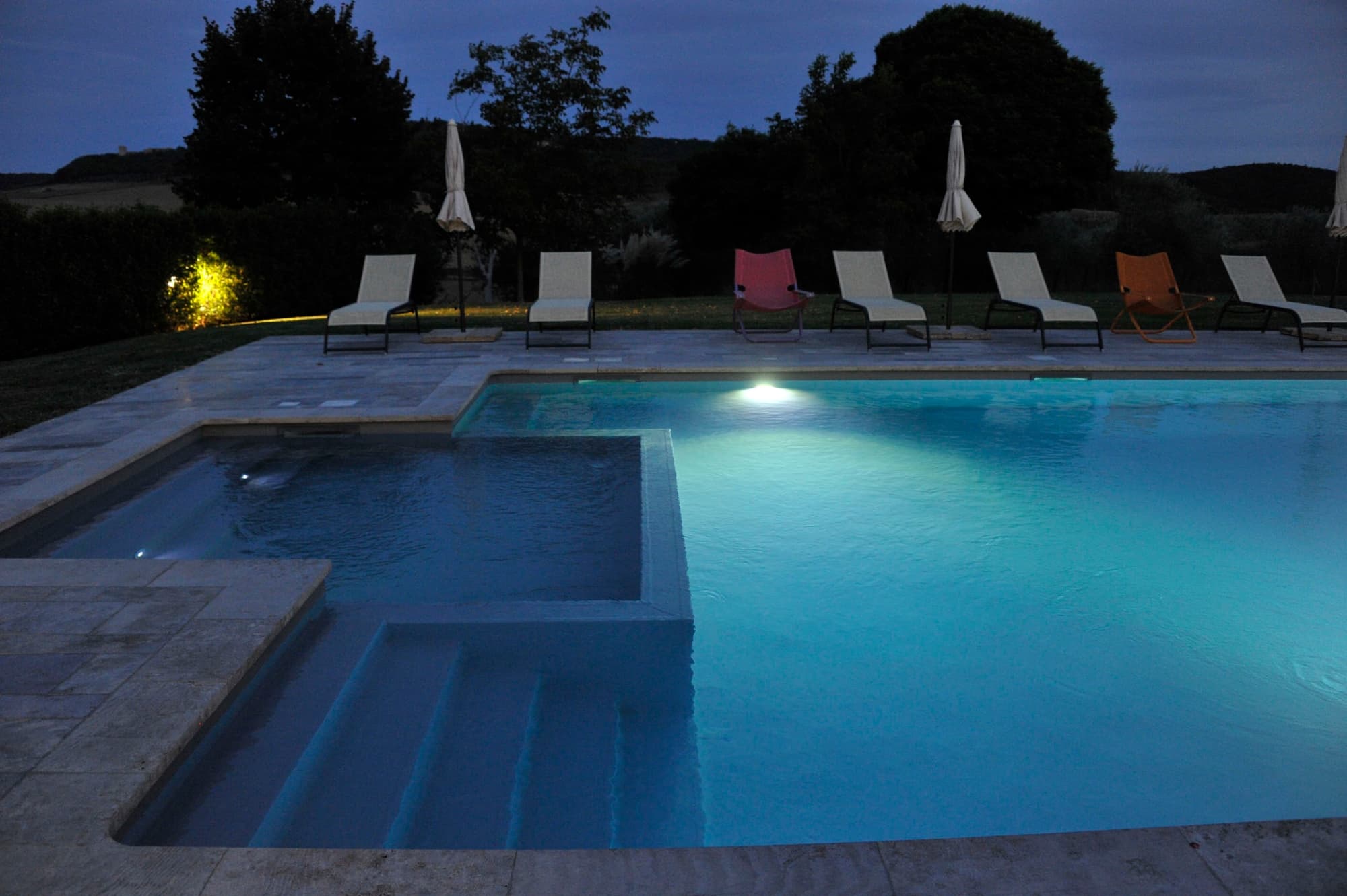 Piscina illuminata di sera con lettini a bordo vasca presso l'agriturismo Podere il Moro in Toscana