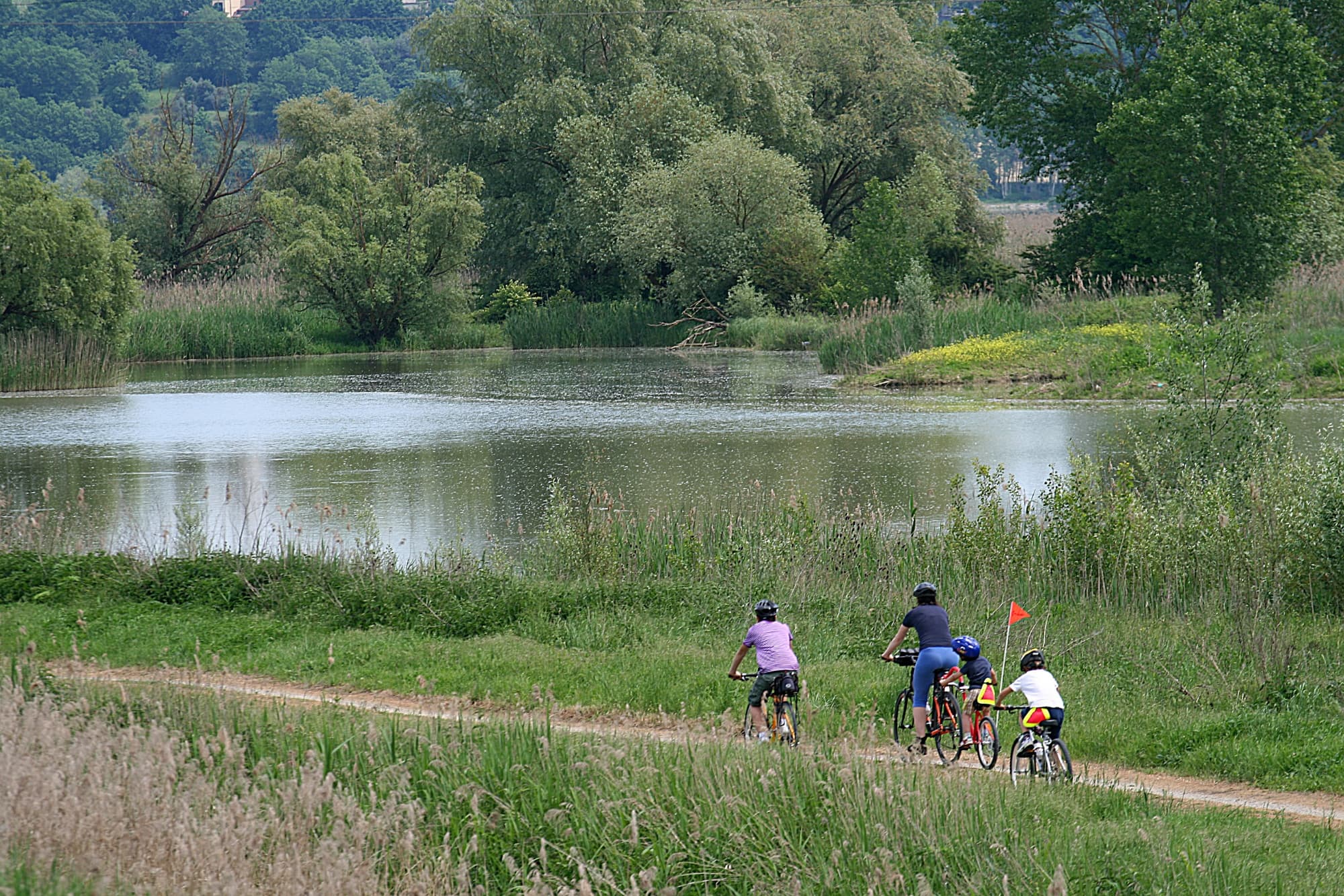 Persone in bicicletta sul Sentiero della Bonifica in Valdichiana, circondato da campi aperti, canali e paesaggi rurali tipici della Toscana.
