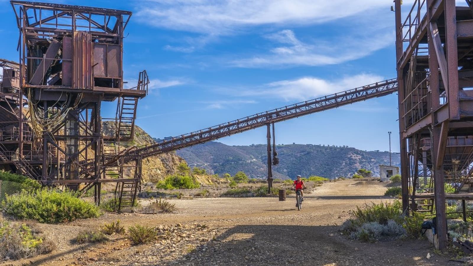 E-bike cyclist in the Calamita mining area with rusty machinery and the sea in the background