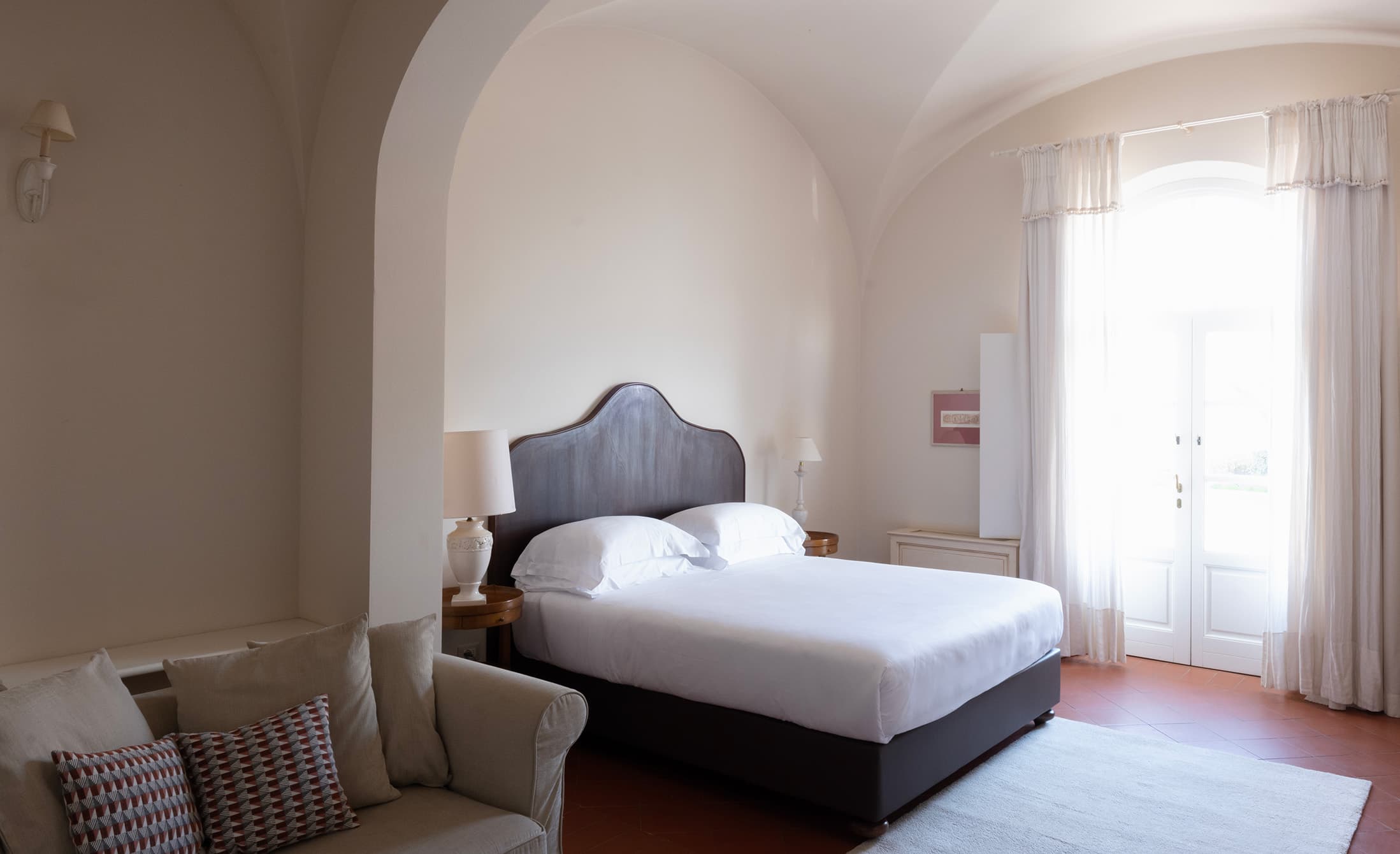 Room with vaulted ceiling, double bed and sofa overlooking a bright French door