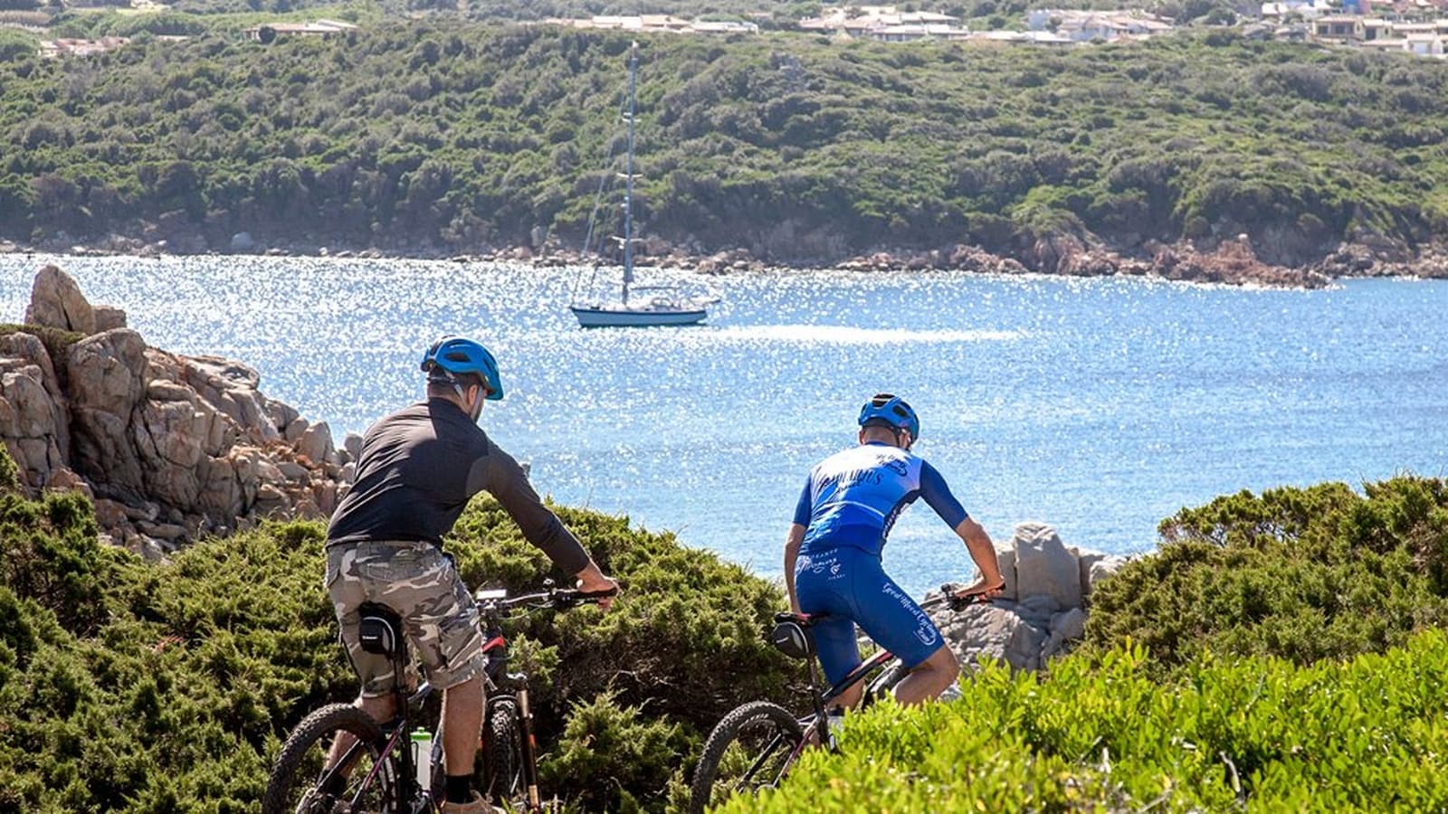 Two cyclists with mountain bikes on a coastal promontory with Mediterranean scrubland and the sea in the background