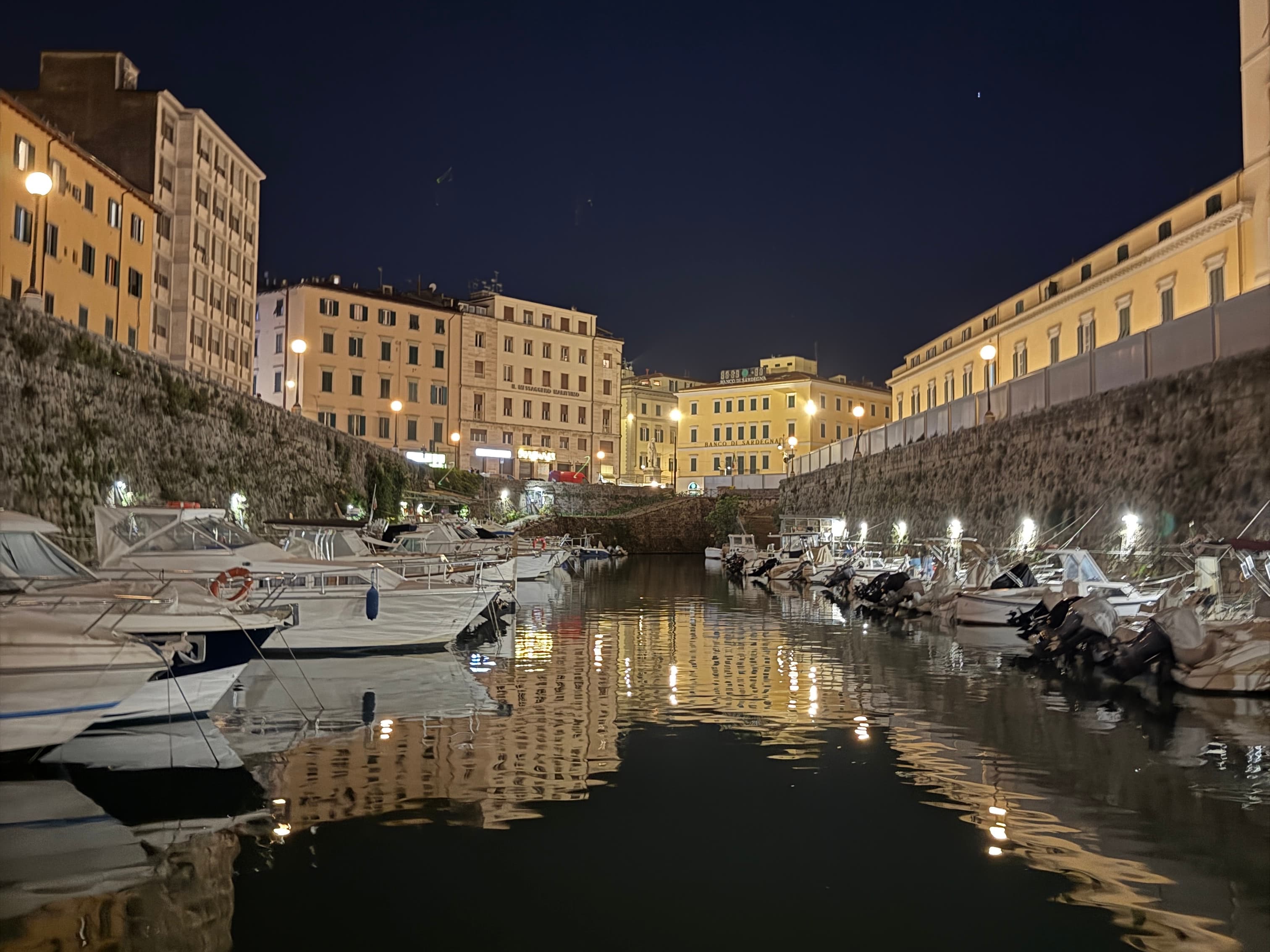 Livorno's urban canal at night with motorboats moored on both banks, illuminated stone walls and historic buildings in the background