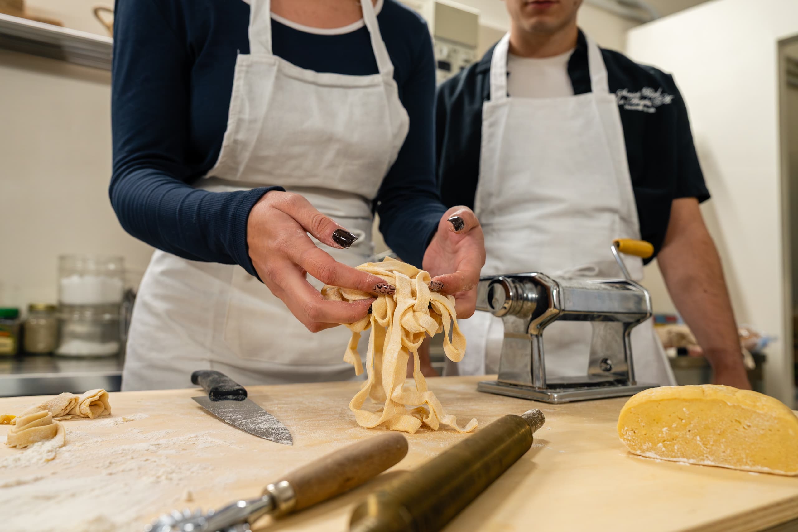 Hands separating fresh tagliatelle on a floured wooden board.